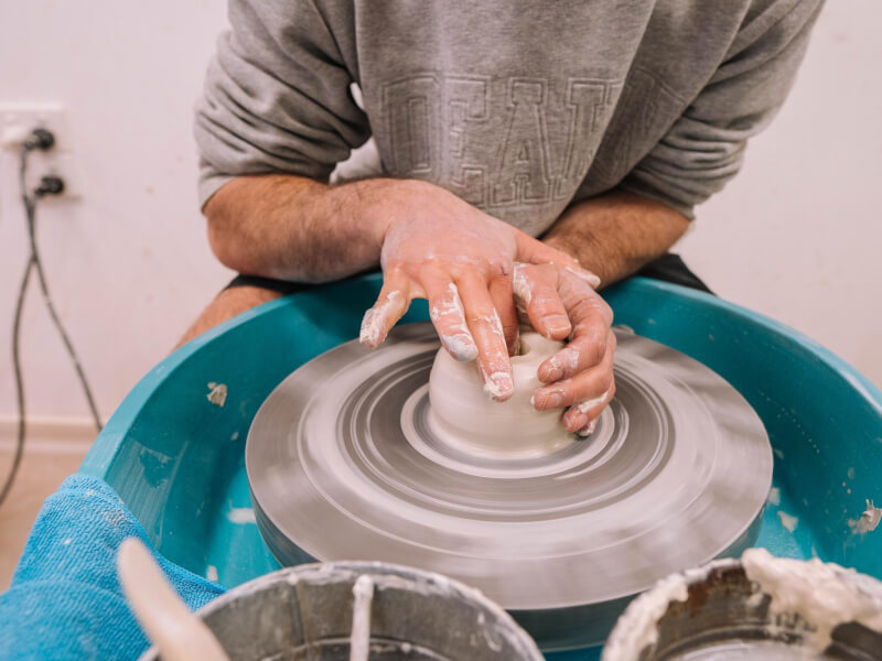 Person shaping pottery at a wheel throwing class